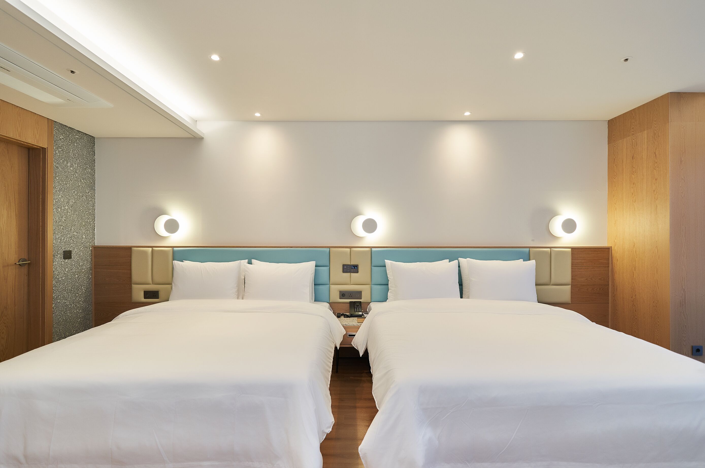 A hotel room with two beds, a wooden wardrobe, a small desk, and a nightstand.