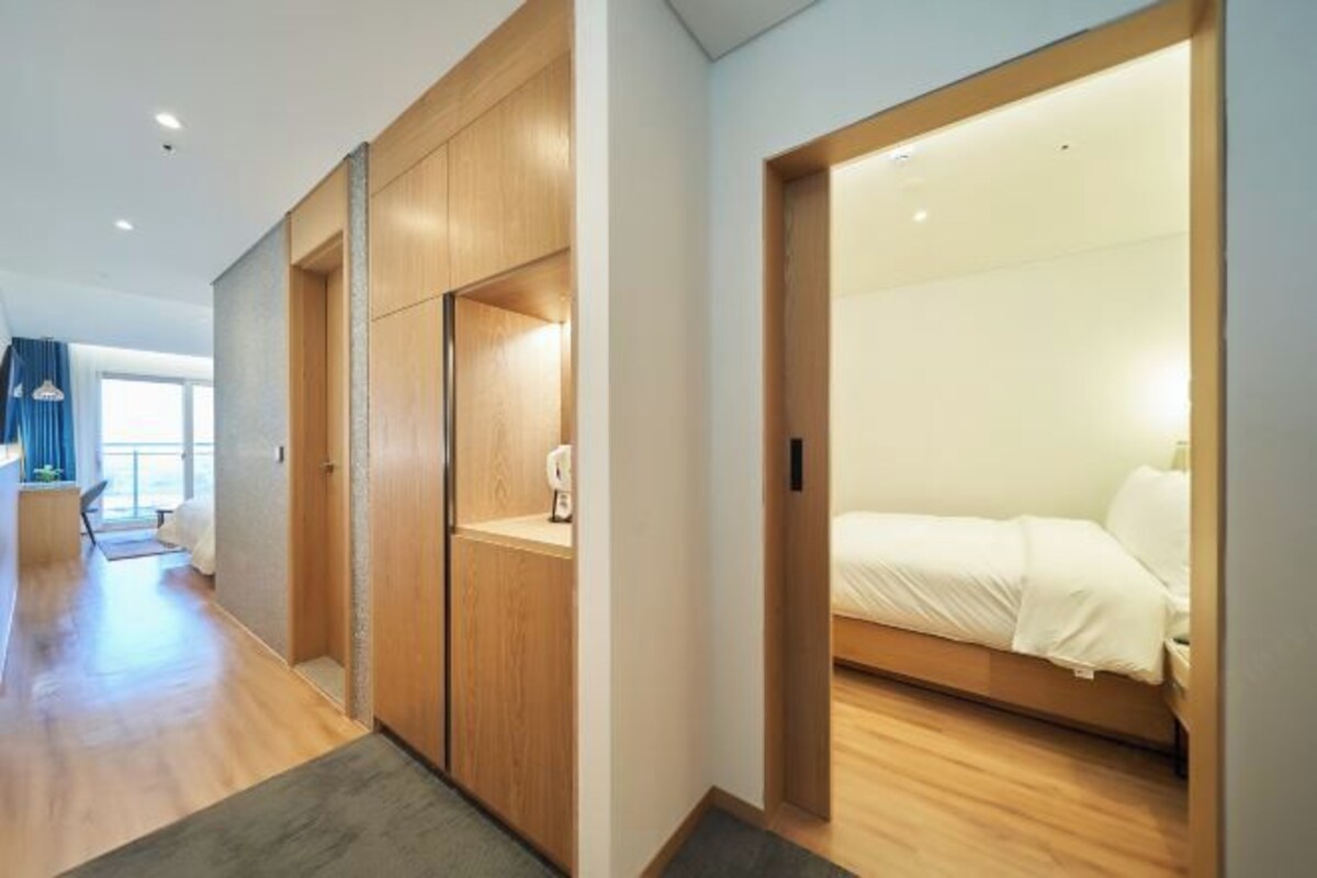 A modern hotel room with a wooden floor, a bed with white bedding, a small bedside table, and a built-in wardrobe.