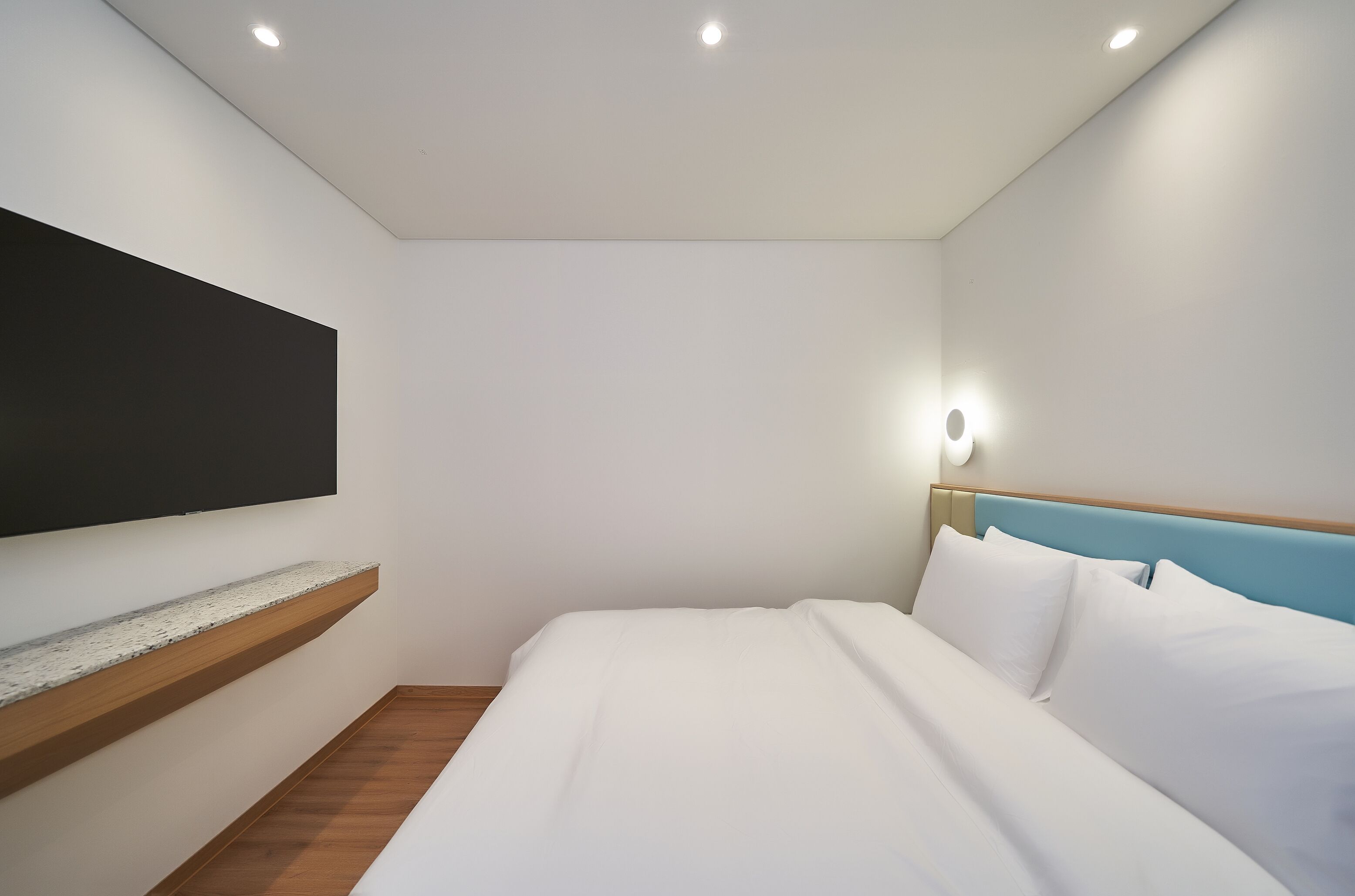 A modern hotel room with a bed, a mounted TV, and a nightstand.