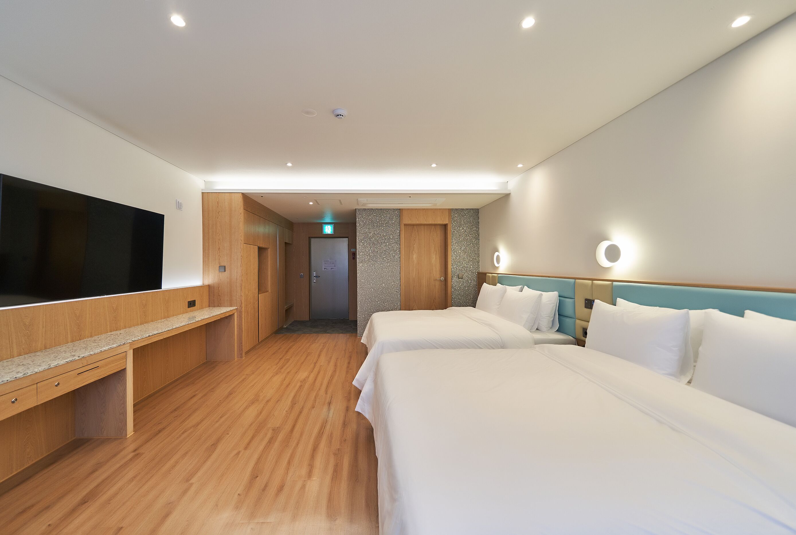 Habitación de hotel con dos camas, televisión, escritorio y baño visible a través de una puerta.
