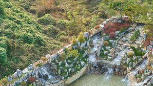 An aerial view of a landscaped area with a small waterfall, seating areas with umbrellas, and a pool. - JN Park Hotel (Incheon)