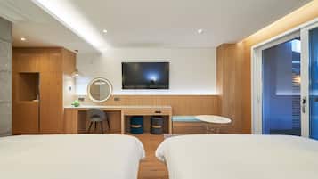 Una habitación de hotel moderna con dos camas, un escritorio, un televisor y una pequeña zona de estar.