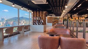 A modern interior with a view of a cityscape, a bookshelf, seating area, and a staircase. - JN Park Hotel (Incheon)