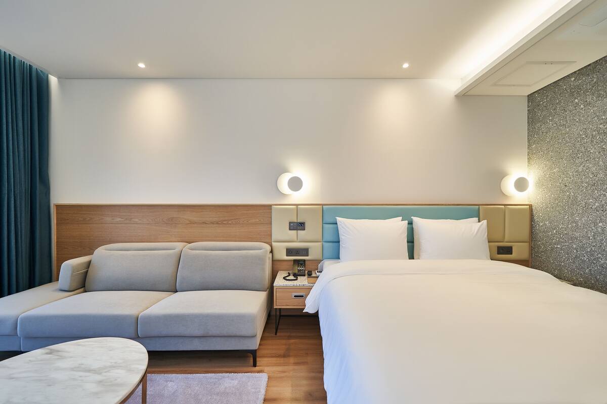 A hotel room with a bed, two sofas, a small table, and a nightstand with a lamp.