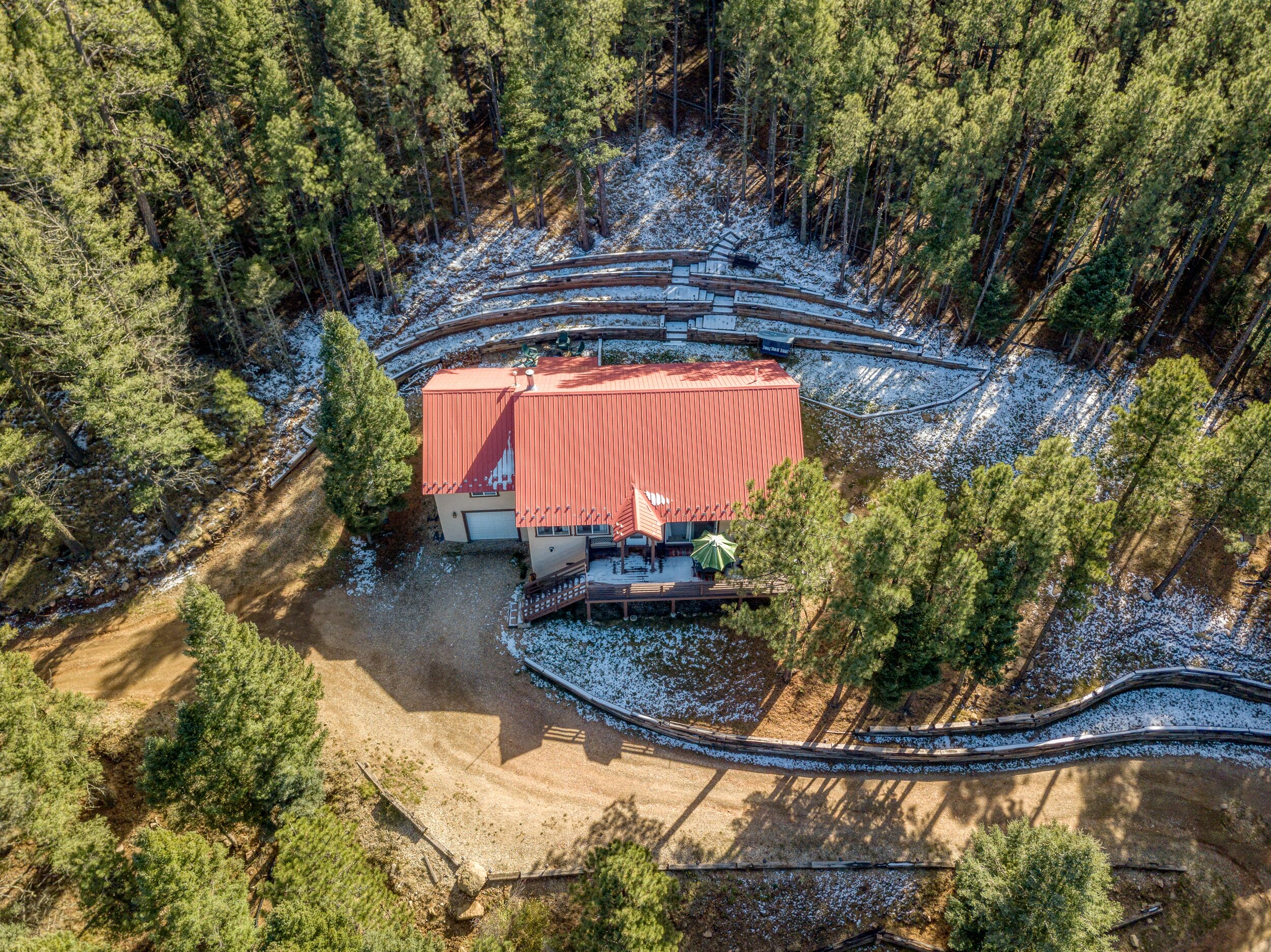Une vue aérienne d’un chalet au toit rouge, entouré d’une forêt dense et d’un sol recouvert de neige.