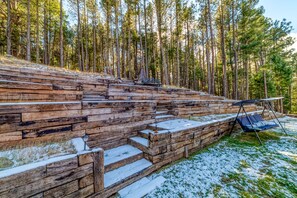 Una escalera de madera conduce a un espacio de descanso con una silla mecedora, rodeado de un área boscosa.