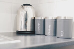 Una encimera de cocina con un hervidor y tres recipientes etiquetados como café, azúcar y té.
