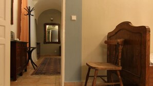 Un couloir avec une chaise en bois, un tapis rouge à motifs et un miroir accroché au mur.