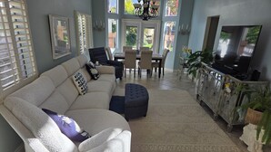 Ein Wohnzimmer mit Ecksofa, Hocker, Esstisch, Stühlen und Fernseher.