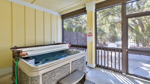 Un bain à remous avec des murs en pierre, un banc en bois et une vue sur les arbres à travers une porte vitrée.