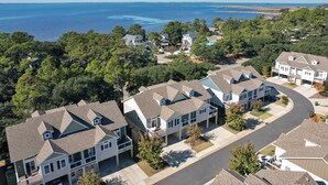 Un quartier résidentiel où les maisons se distinguent par leurs toits à pignons et leurs grandes fenêtres, le tout étant entouré d’arbres et offrant une vue sur l’océan.