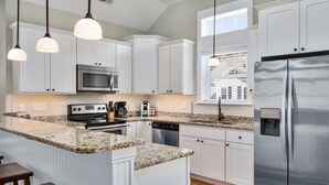 Une cuisine moderne avec des meubles blancs, des plans de travail en granit, des appareils électroménagers en acier inoxydable et des luminaires suspendus.
