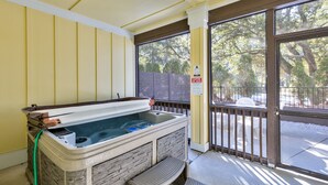 A hot tub with stone walls, a wooden bench, and a view of trees through a glass door.