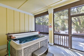 A hot tub with stone walls, a wooden bench, and a view of trees through a glass door.