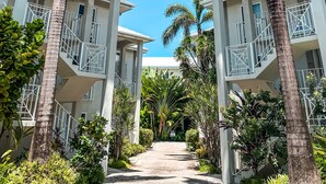 A hotel with a central pathway flanked by palm trees and a two-story building with balconies. - Luxury condo steps from one of the world's best beaches. (George Town)