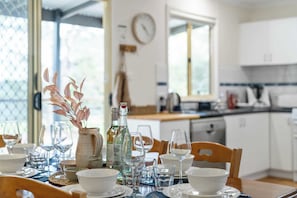 A dining table set with glassware, plates, and a vase with dried flowers.
