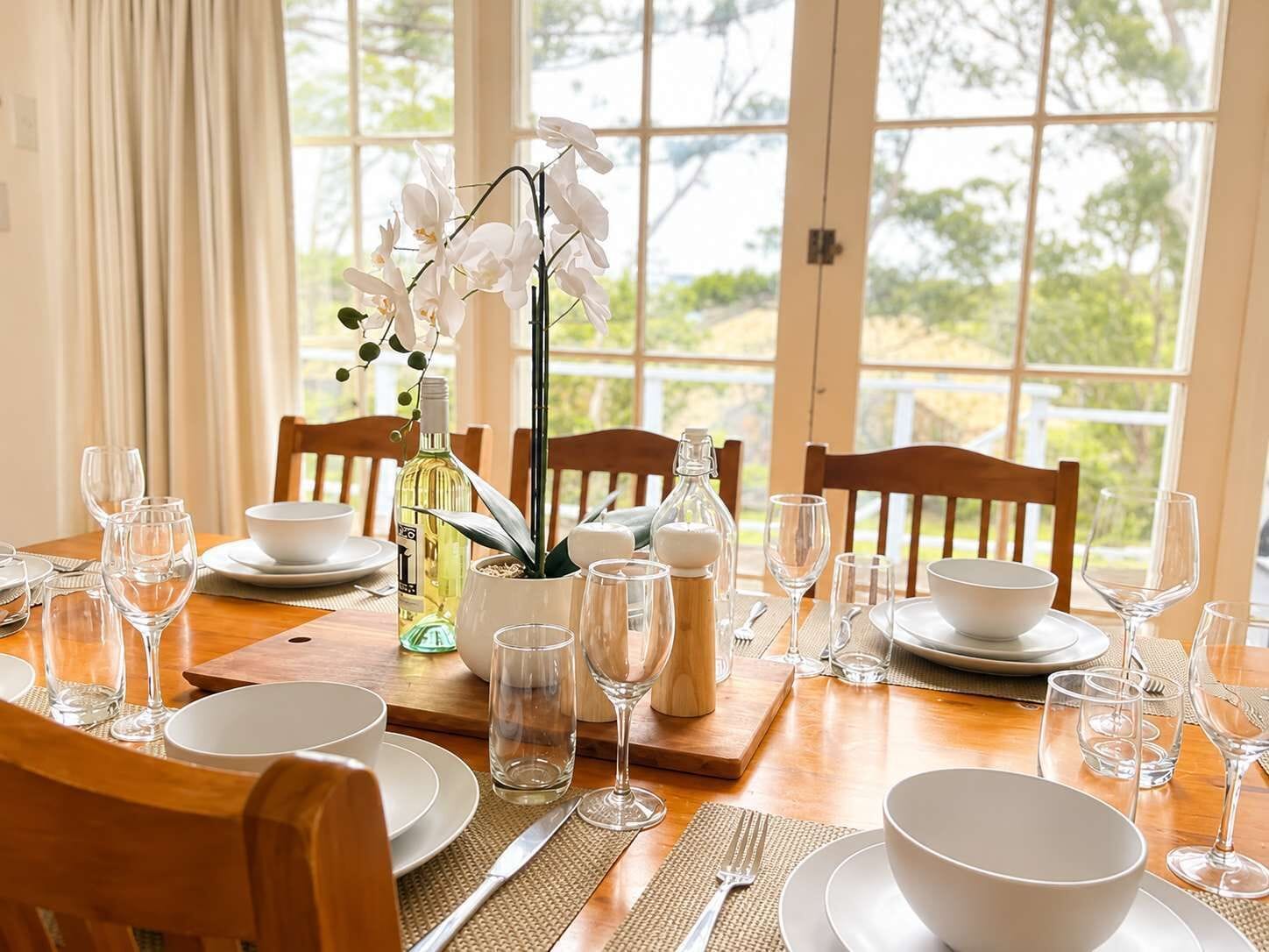 A dining table set for a meal with white plates, clear glasses, and a centerpiece of white orchids.