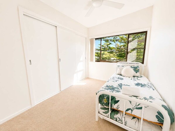 A bedroom with a bed, a window with a view of greenery, and a ceiling fan.