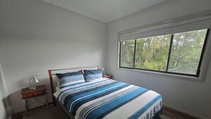 Une chambre à coucher avec un lit, une table de chevet, une lampe et une fenêtre donnant sur des arbres.