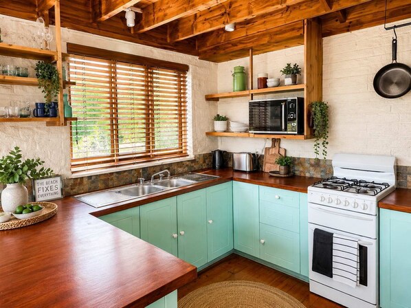 Una cocina con vigas de madera, estufa, horno microondas y pileta.