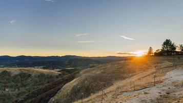 A hilly landscape with a sunset, a fenced area, and distant buildings.