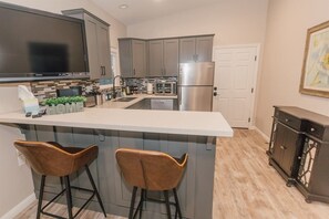 A modern kitchen with a large island, bar stools, stainless steel appliances, and a flat-screen TV.