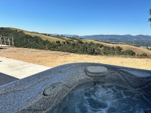 Una vasca idromassaggio con pannello di controllo, immersa in una vista di dolci colline e cielo sereno.