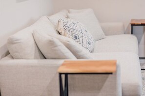 A neutral-colored sofa with a patterned throw pillow and a wooden side table.