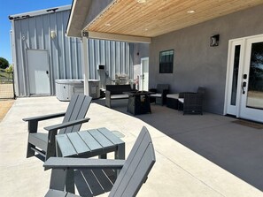 An outdoor patio with Adirondack chairs, a table, and a grill area.