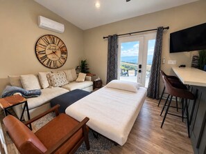 A modern hotel room with a large bed, a sofa, a TV, and a view of the outdoors.