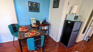 A compact kitchen with a dining area, featuring a microwave, refrigerator, and a small table set with dishes. - Luxurious, Private Suite (Hilo)