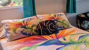 A bed with colorful floral bedding and a painting above it. - Luxurious, Private Suite (Hilo)