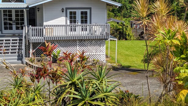 A white house with a balcony, surrounded by lush greenery and a well-maintained lawn. - Luxurious, Private Suite (Hilo)