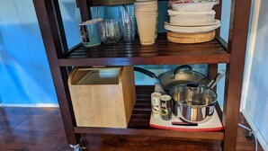 A wooden kitchen cart with shelves holding plates, cups, and a pot. - Luxurious, Private Suite (Hilo)