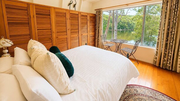 Une chambre dotée d’un grand lit, offrant une vue sur un lac, et comprenant un coin repas avec une table et des chaises.