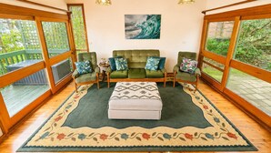 Une pièce avec un canapé vert, deux fauteuils, un tapis à motifs et un tableau accroché au mur.