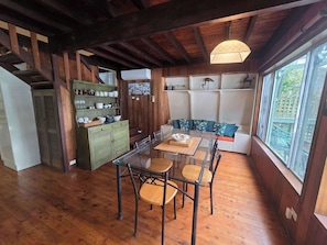 Interior em madeira com uma mesa de jantar, cadeiras, um armário verde e uma janela com vista.