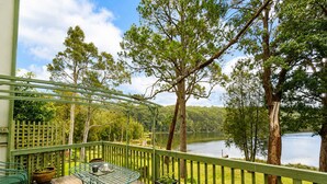 Une terrasse en bois avec une rambarde en métal vert, une table et des chaises, donnant sur un lac bordé d’arbres.