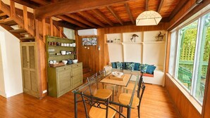 Un intérieur en bois comprenant une table à manger, des chaises, un canapé et une fenêtre donnant sur un paysage verdoyant.
