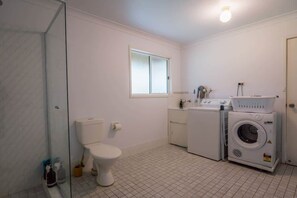 Un baño con inodoro, cabina de ducha de vidrio, lavadora y secadora.