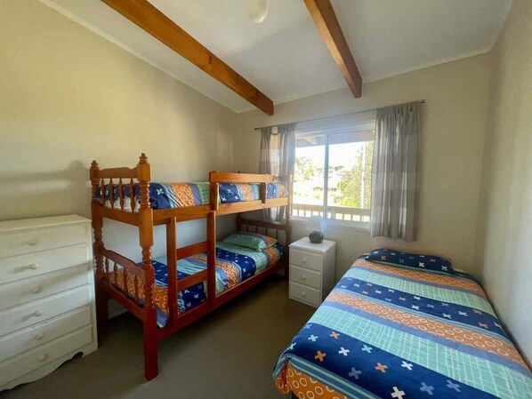 Un dormitorio con literas, un aparador, una mesita de noche y una ventana con cortinas.