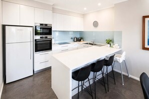 A modern kitchen with white cabinetry, a built-in oven, a refrigerator, and a bar area with stools.