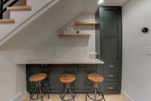 A kitchen with a white countertop, three wooden stools, and a dark green cabinet.