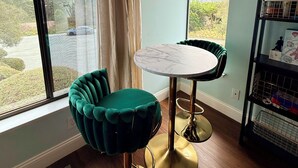 Una habitación con una mesa redonda, dos sillas, una estantería y vistas a una carretera y zonas verdes al exterior.