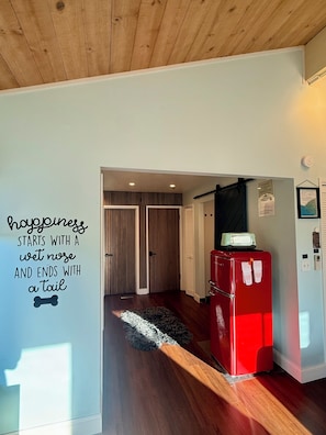 A hallway with a wooden ceiling, a red refrigerator, a wall with a humorous quote, and a striped door. - Modern 1BR Carmel Escape: Dog Friendly En-suite, Valley Views & Mins to Downtown (Carmel-by-the-Sea)