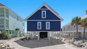 A two-story beach house with a dark blue exterior, white trim, and a balcony on the upper floor. - Modern Beach Front Home with Volleyball net | Summer's Point by Kaiser Vacation Rentals. (Gulf Shores)