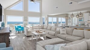 A spacious living room with large windows, a high ceiling, and a view of the ocean. - Modern Beach Front Home with Volleyball net | Summer's Point by Kaiser Vacation Rentals. (Gulf Shores)