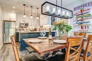A modern kitchen with a central island, pendant lights, and a dining area with a wooden table and chairs.