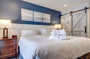 A hotel room with a bed, two bedside tables with lamps, a large artwork on the wall, and a sliding barn-style door. - Greystone Lodge 329 Ski-in/Out by Acer Vacations (Whistler)