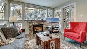 Una sala de estar con chimenea, un sofá, un sillón rojo y un televisor.